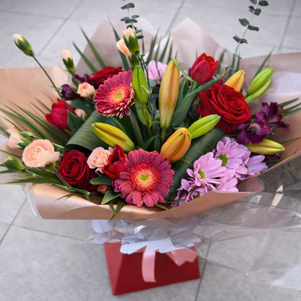 Bouquet of colorful flowers wrapped in brown paper on a light gray floor.